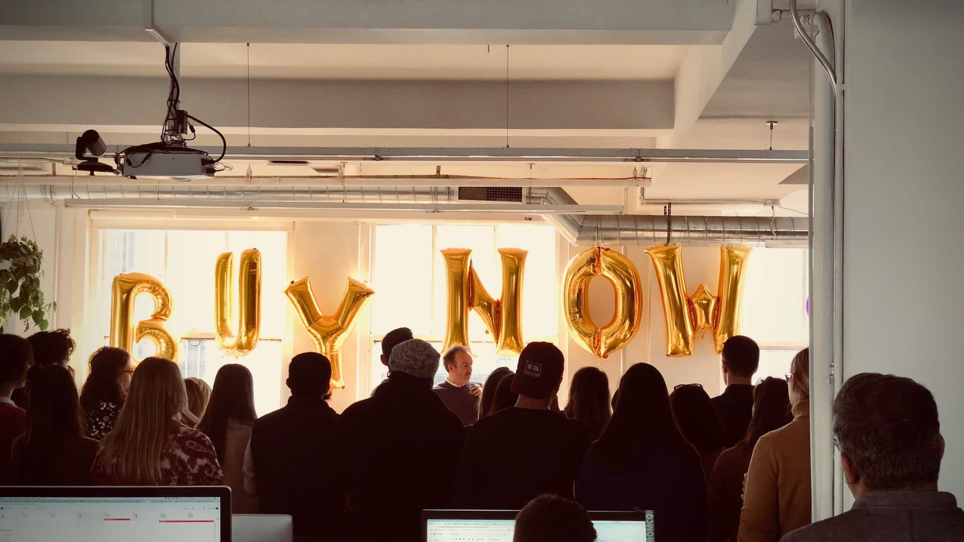Photo of the Artsy office with people celebrating in front of balloons that spell out BUY NOW